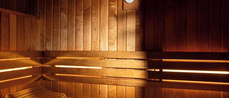 A sauna with wooden benches and benches, a bench with a towel, and a wall-mounted thermometer.