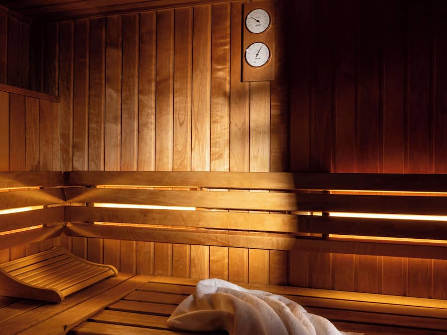 Eine Sauna mit Holzbänken, eine Bank mit einem Handtuch und ein an der Wand befestigtes Thermometer.