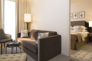 A modern hotel room with a sofa, a chair, a small table, and a bed with a headboard.