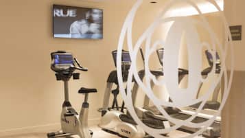 Un gimnasio con cintas de correr y una bicicleta estática, una pantalla de televisión y el letrero de un sauna.