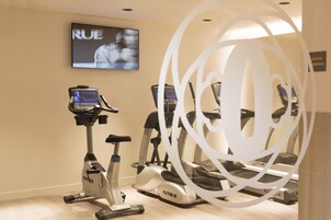Un gimnasio con cintas de correr y una bicicleta estática, una pantalla de televisión y el letrero de un sauna.