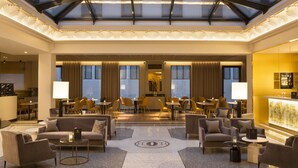 Un amplio vestíbulo de hotel con techo alto, una zona de estar central y una recepción.