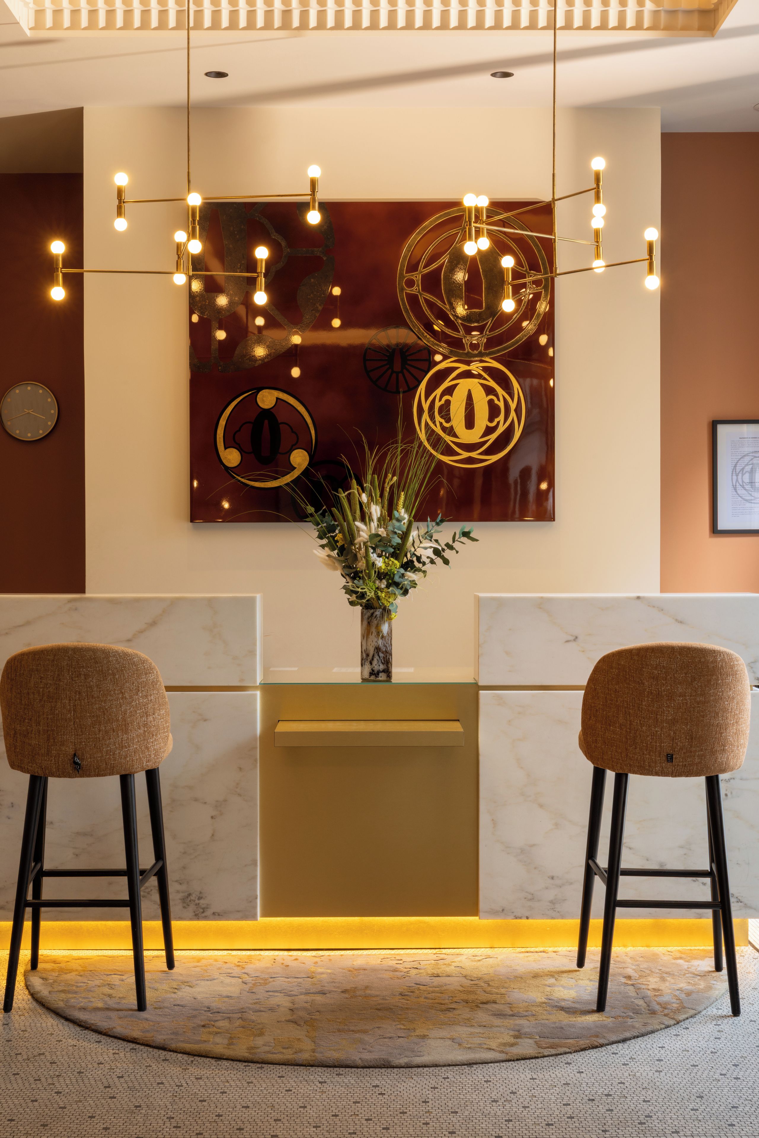 A reception area with a marble reception desk, two bar stools, a wall-mounted clock, and a decorative wall piece.