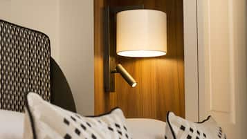 Una habitación de hotel con una puerta de madera, una lámpara fijada a la pared y almohadas estampadas.
