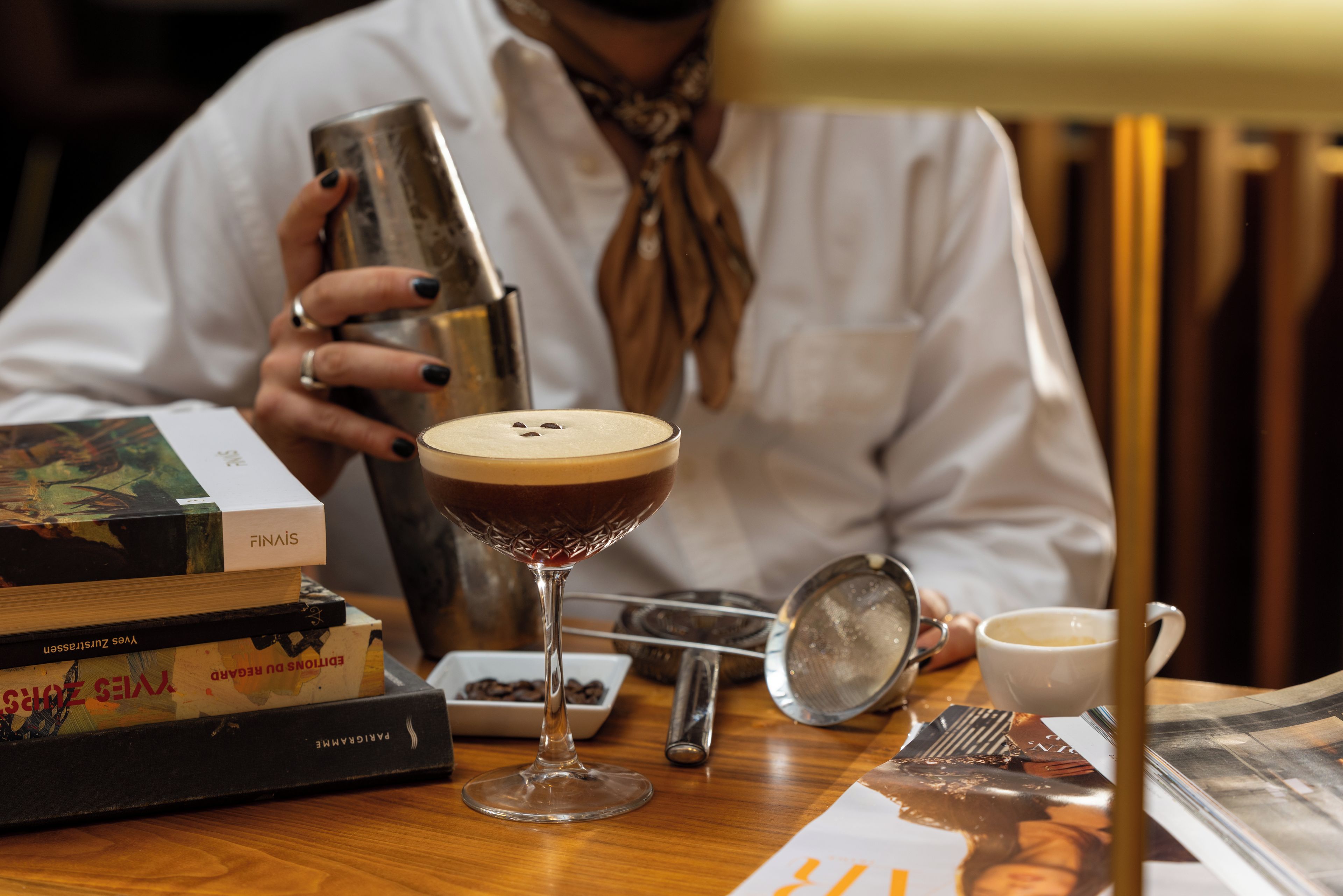 A person pouring a drink into a glass, with books and a coffee cup on the table.