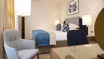 A hotel room with a bed, two bedside lamps, a chair, a desk, and a large mirror.