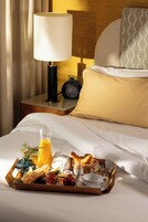 A neatly made bed with a tray of breakfast items, a bedside table with a lamp and a digital clock, and a patterned pillow.