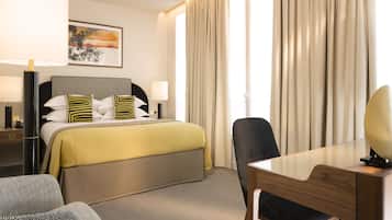A hotel room with a bed, a desk, a chair, a lamp, and a painting on the wall.