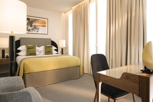 Una camera d'albergo con un letto, una scrivania, una sedia, una lampada e un quadro appeso al muro.