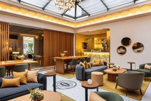 A spacious lobby with a high ceiling, a seating area with sofas and chairs, a bar area, and a reception desk.