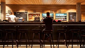 A bar area with wooden ceiling, bar stools, and a bartender. - Moxy Berlin Ostbahnhof (Berlin)