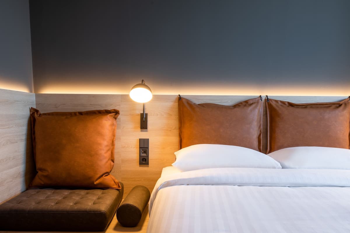 A hotel room with a bed, two pillows, a nightstand, a lamp, and a wooden headboard.