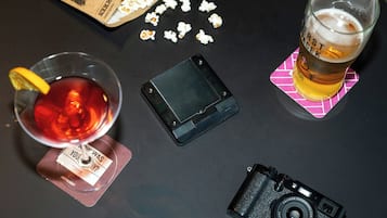 Une table avec un verre de bière, un appareil photo, un téléphone intelligent et du pop-corn éparpillé.