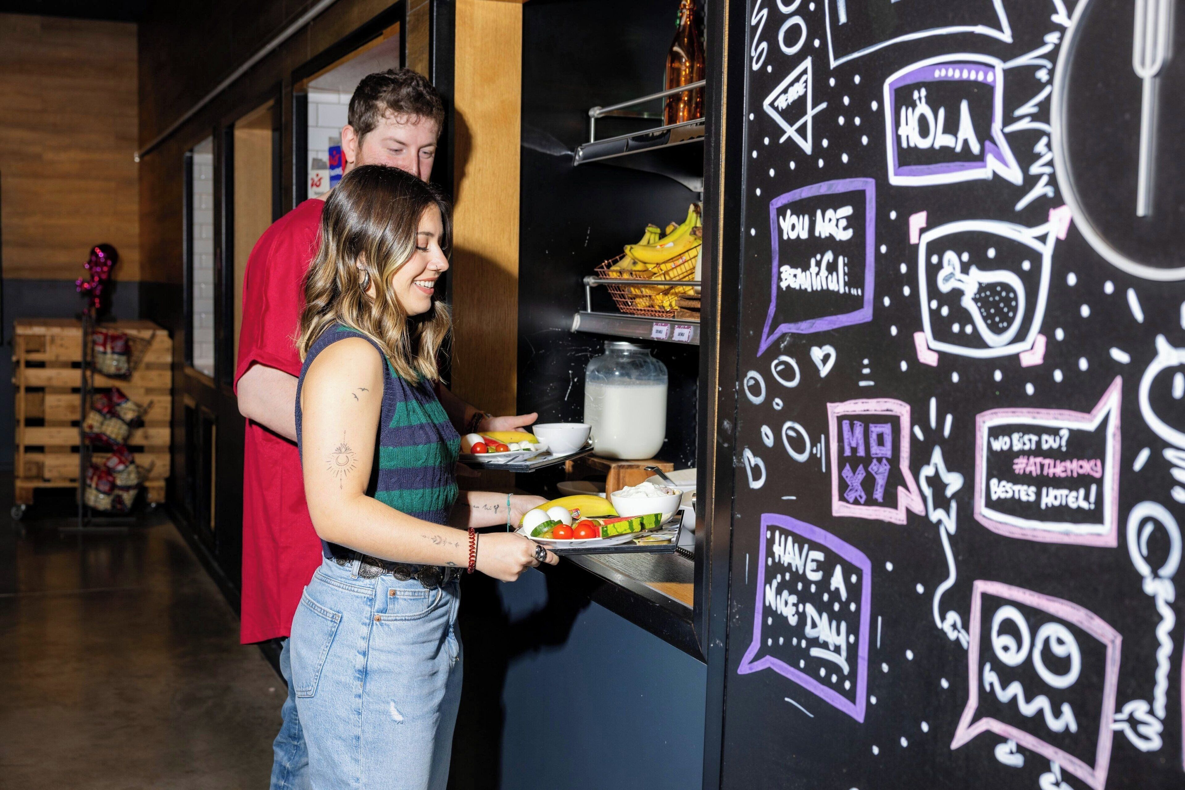 A woman serving food from a counter with a chalkboard wall featuring doodles and text.