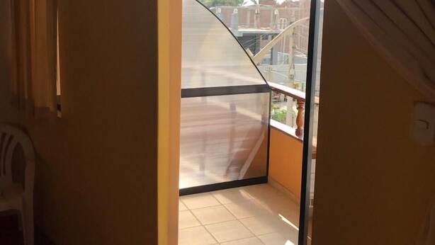 A room with a sliding glass door leading to a balcony with a view of buildings and a clear sky.
