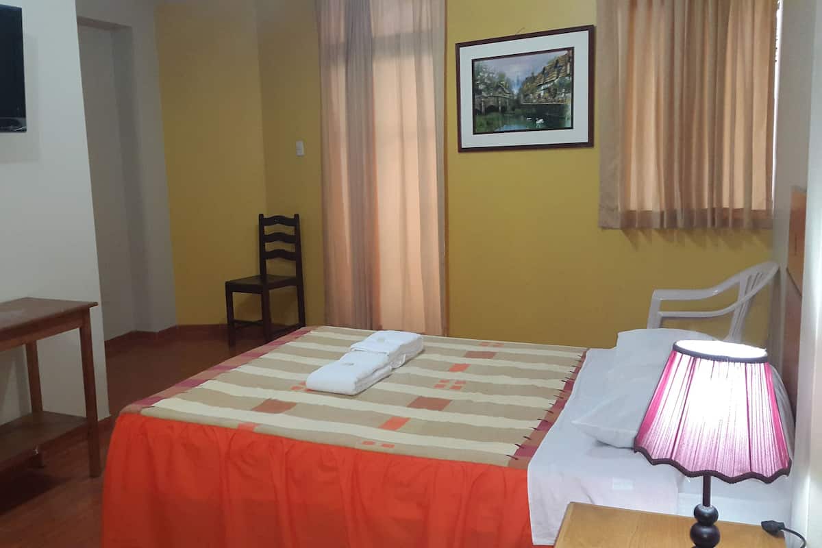 Una habitación de hotel con una cama, una silla, una mesita, una lámpara y un cuadro en la pared.