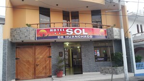 A hotel named 'Hotel Sol de Huanchaco' with a large sign, a wooden entrance door, and a balcony.