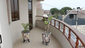 A balcony with two potted plants, a tiled floor, and a railing with a sign.