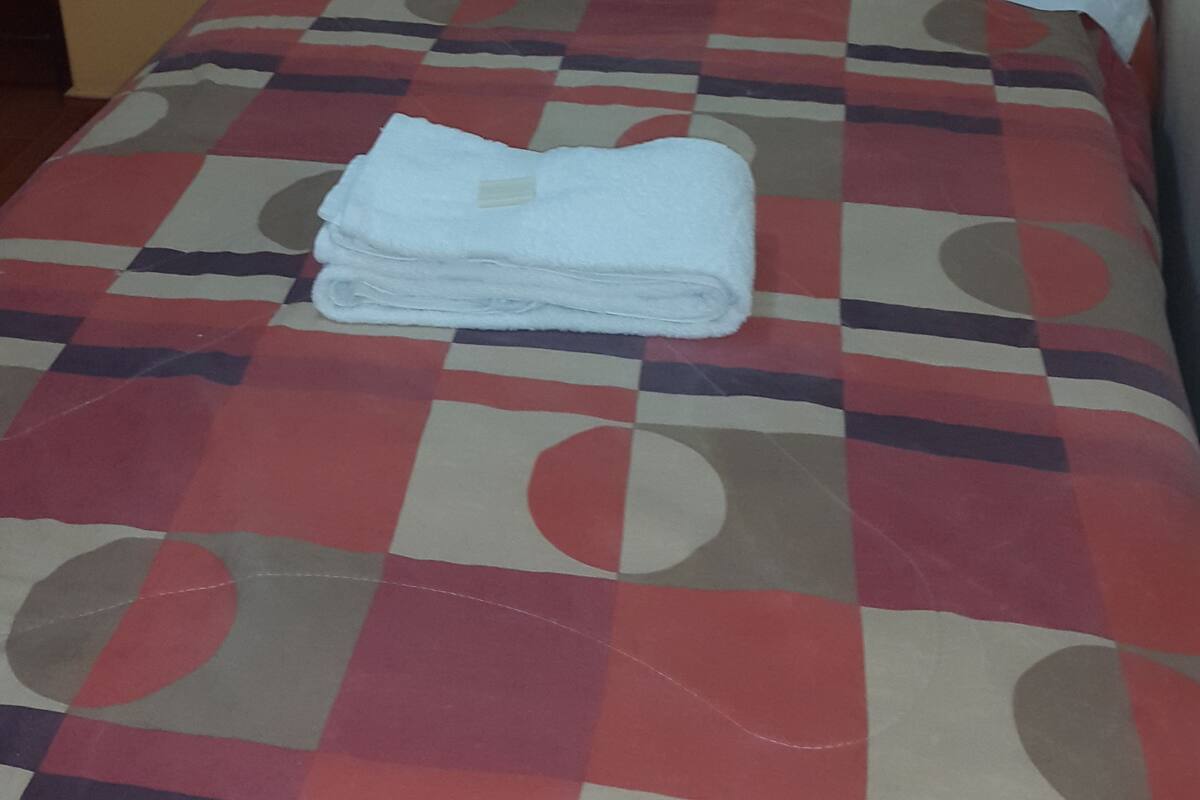 Una cama con una colcha a cuadros y una toalla blanca doblada.