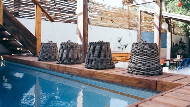 Un espace piscine agrémenté de paniers en osier disposés le long du bord, d’une terrasse en bois et d’une structure en forme de pergola.