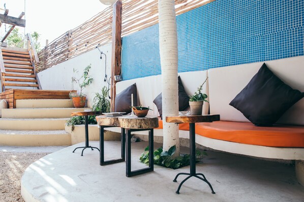 A sunlit outdoor seating area with a wooden staircase, potted plants, and a blue-tiled wall.