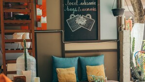 Une pièce chaleureuse avec un canapé en bois, des coussins, une petite table sur laquelle est posé un vase, et un tableau noir servant de panneau publicitaire pour la vente de miel et d’artisanat local.