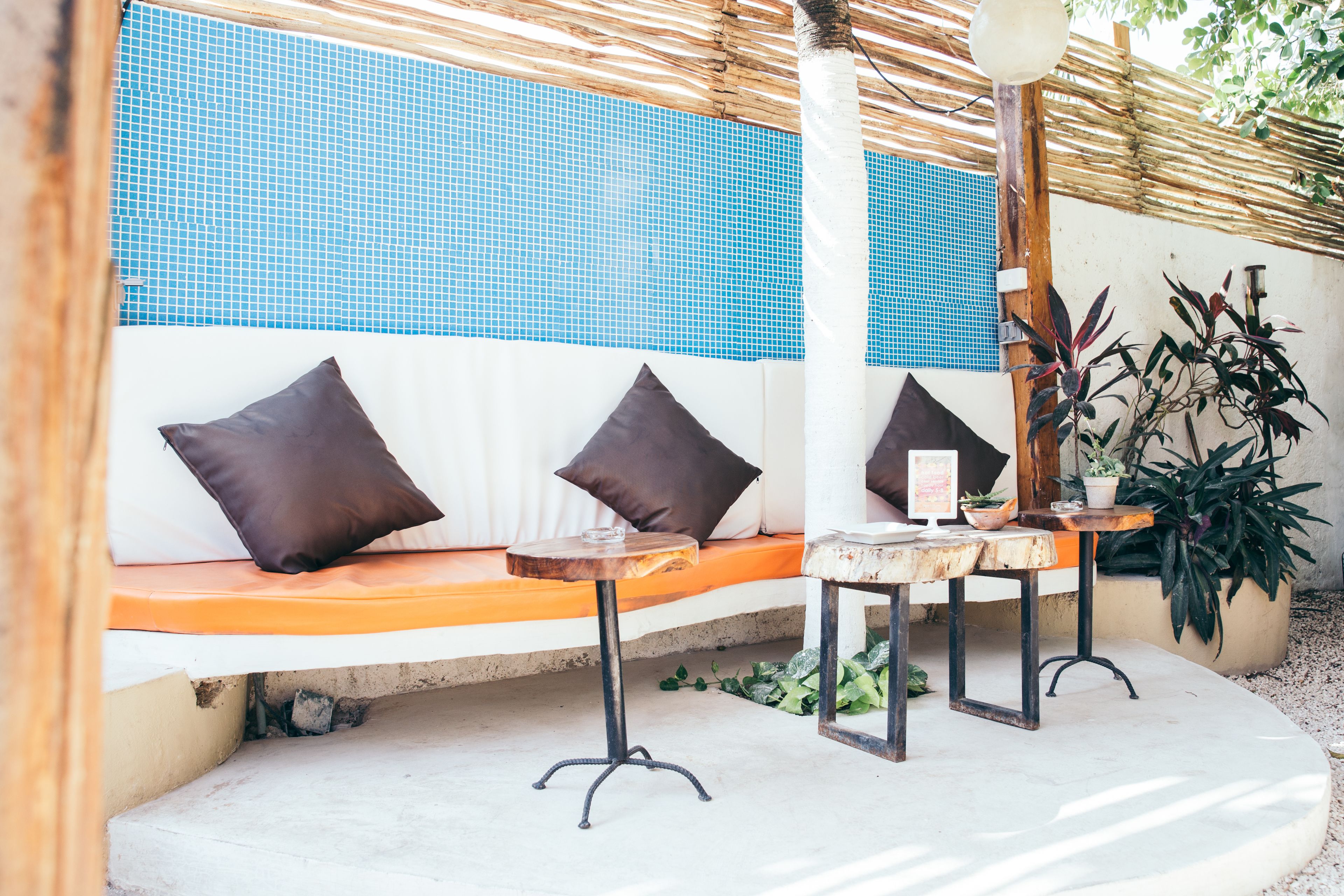 Un área de descanso con un banco y dos mesas, una pared de azulejos azules, y plantas en macetas.