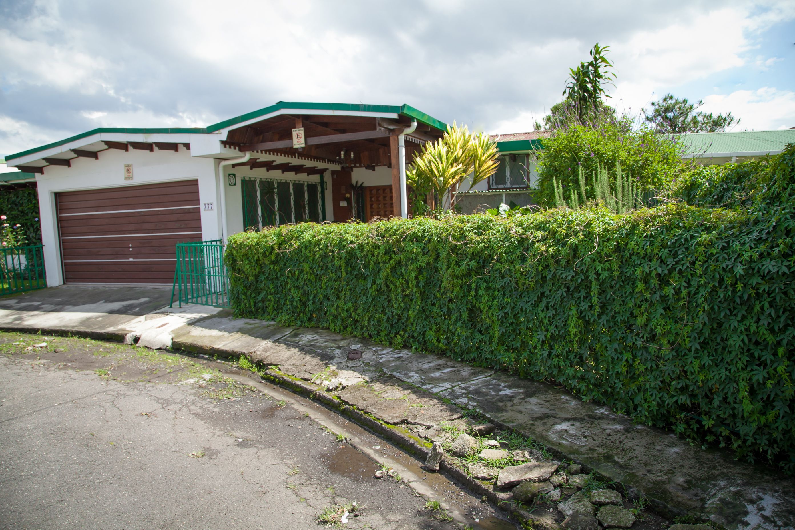 A residential building with a garage, a covered porch, and a well-maintained hedge.