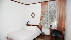 Une chambre à coucher avec un lit, un bureau avec une chaise, une lampe et une fenêtre avec des rideaux.