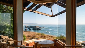 A room with a large glass window overlooking a coastal view, featuring a wooden ceiling and wicker furniture. - The Inn at Newport Ranch (Fort Bragg)