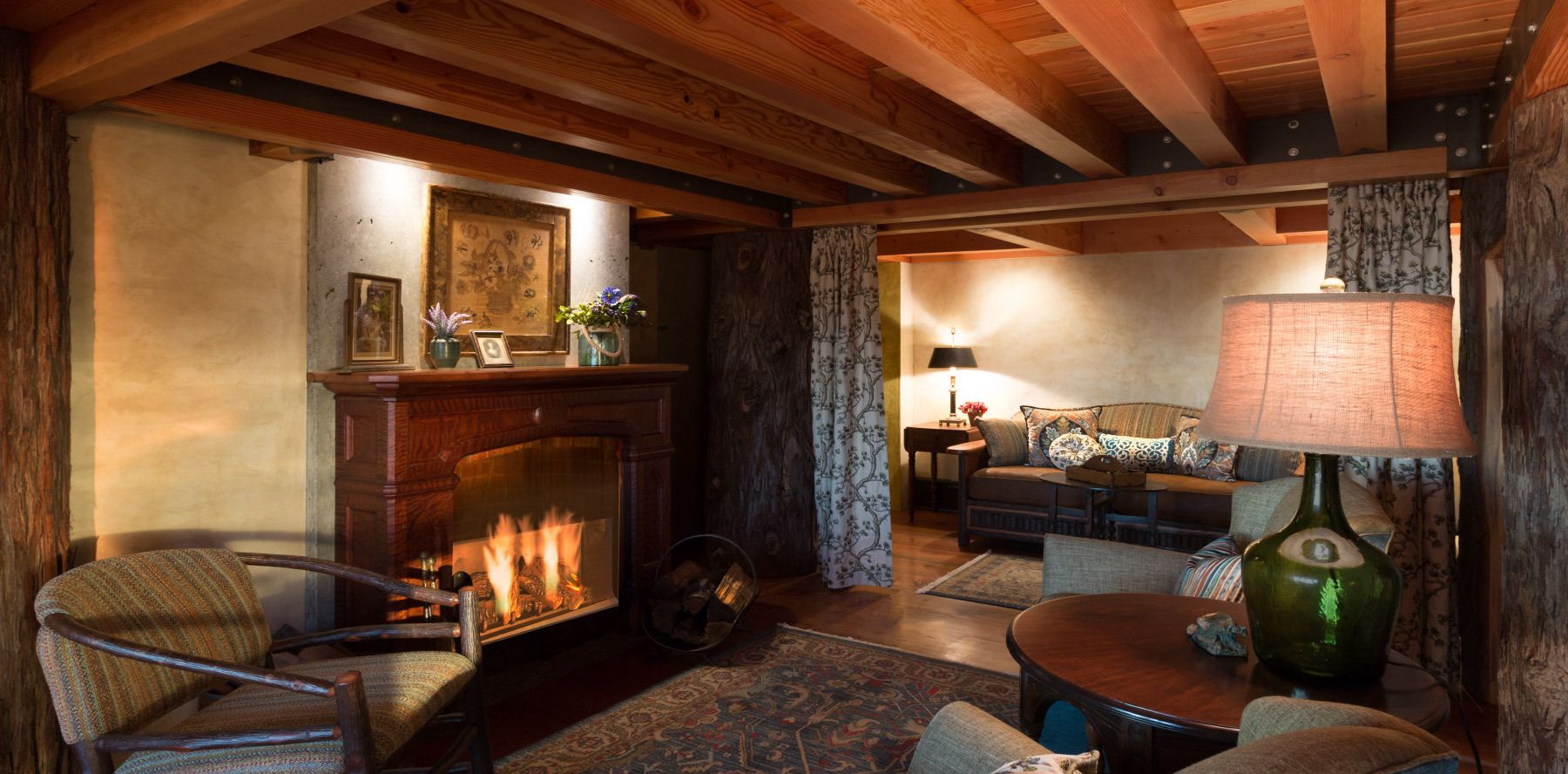 A cozy living room with a fireplace, wooden beams, a sofa, and a lamp.