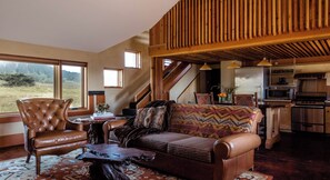 A spacious living area with a leather armchair, a patterned sofa, a wooden coffee table, and a view of the outdoors.