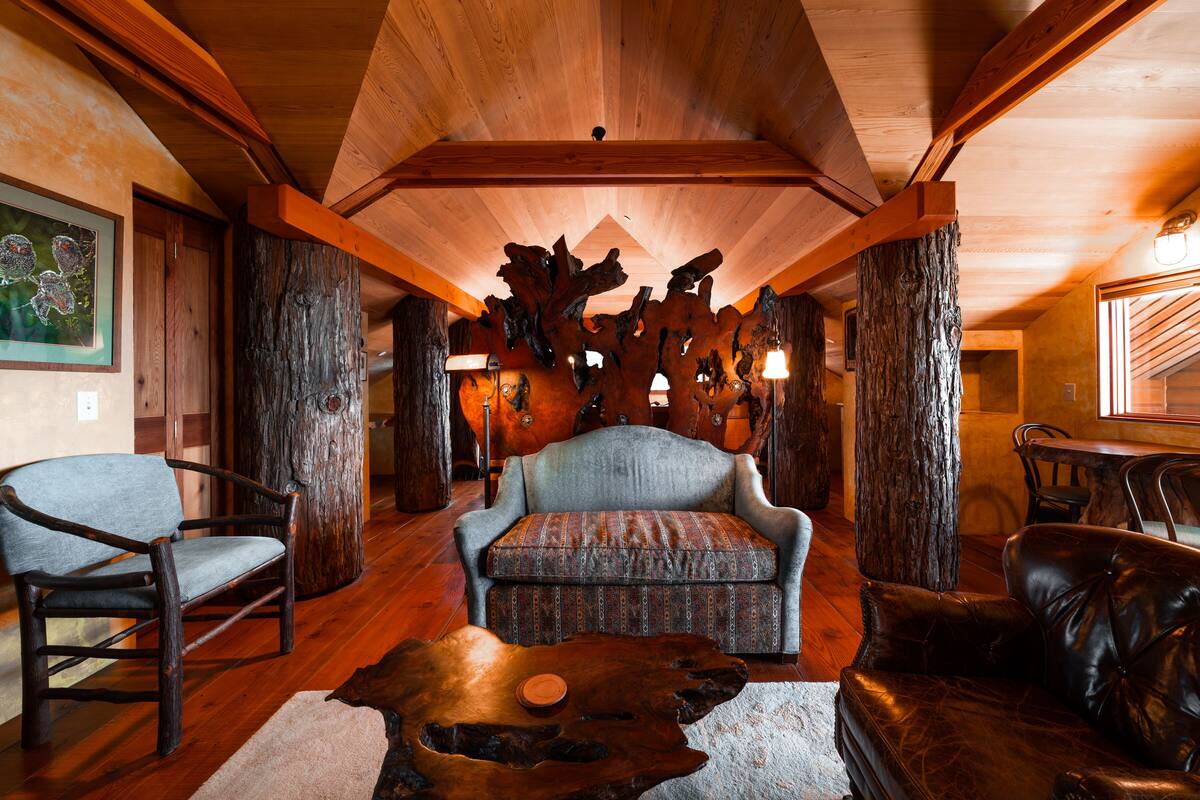 Un interior rústico con techo de madera, un sofá estampado, sillones de cuero y una escultura de madera original.