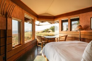 A bedroom with a large bed, wooden walls, and a view of the landscape through large windows.