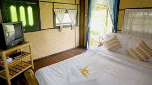 A hotel room with a bed, a TV on a wooden stand, and a window with curtains.