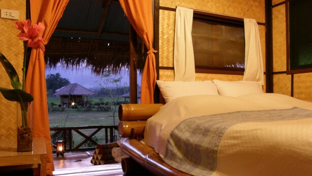 A bedroom with a bed, curtains, a window, and a view of the outdoors.