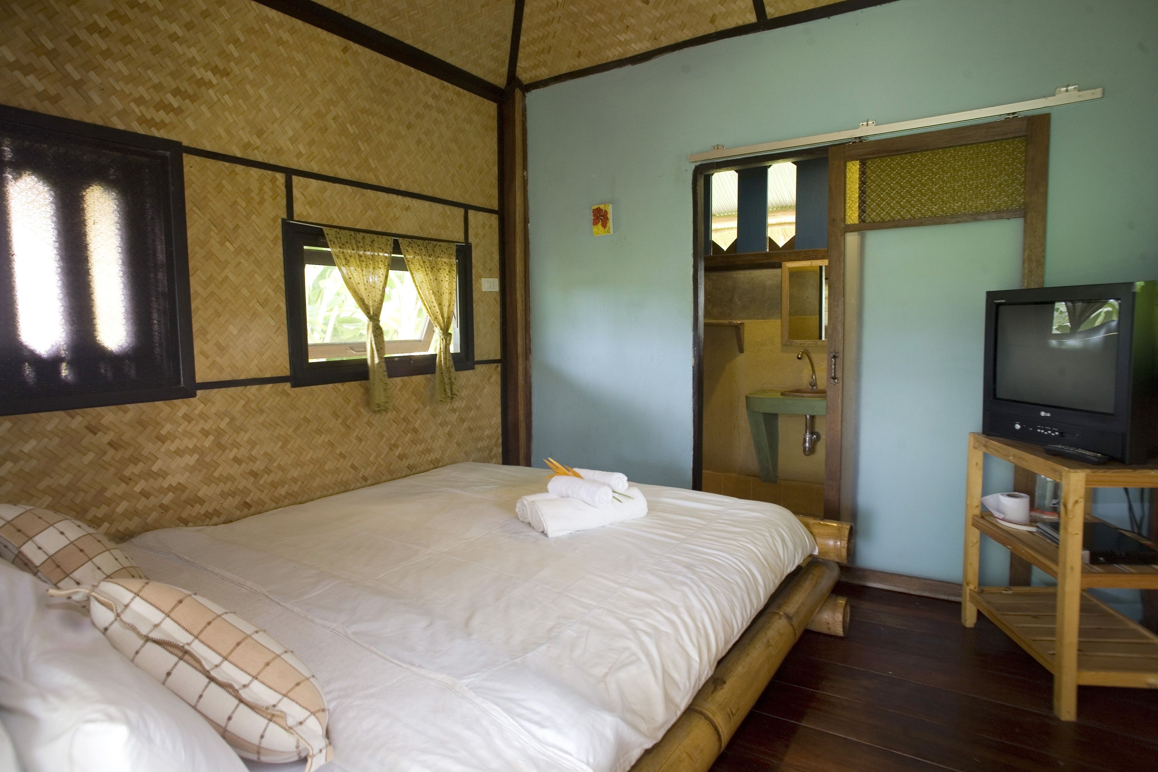 A room with a large bed, a television on a wooden stand, and a bathroom visible through a glass door.