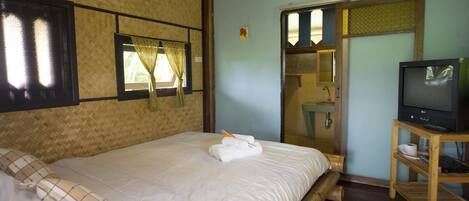 A room with a large bed, a television on a wooden stand, and a bathroom visible through a glass door.