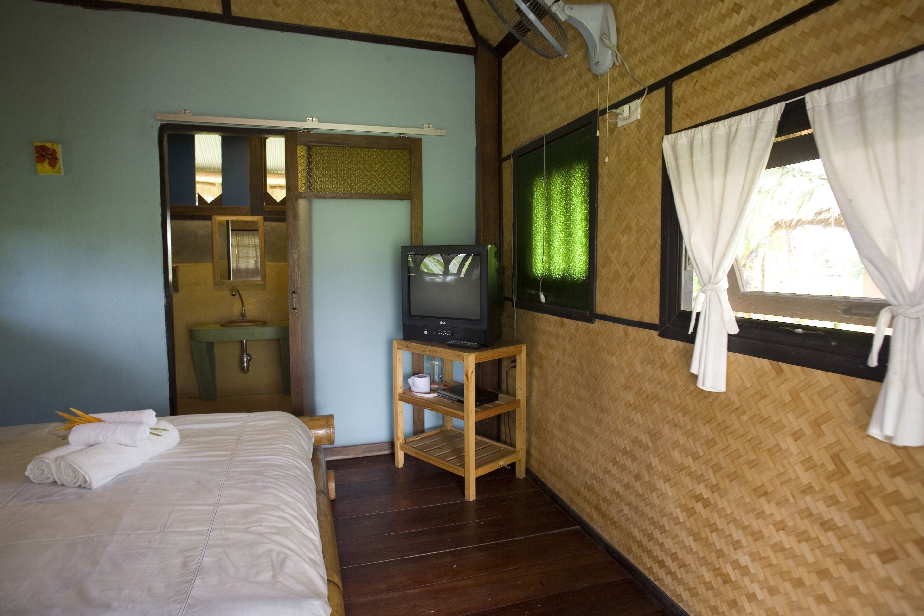 A room with a bed, a television on a wooden stand, a window with curtains, and a bathroom visible through an open door.