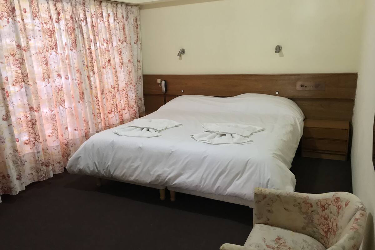 Une chambre d’hôtel avec un lit, une chaise et un rideau.