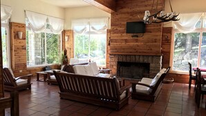 A spacious living room with a fireplace, wooden walls, and large windows. - Alun Nehuen (San Carlos de Bariloche)