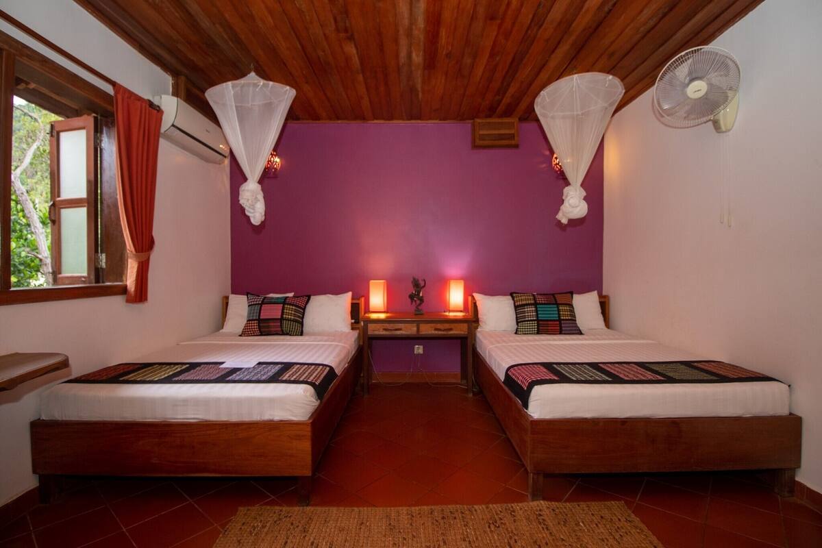 A room with two wooden beds, a nightstand, a window with curtains, and a ceiling fan.