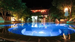 Una piscina nocturna amb gandules i un edifici al fons.