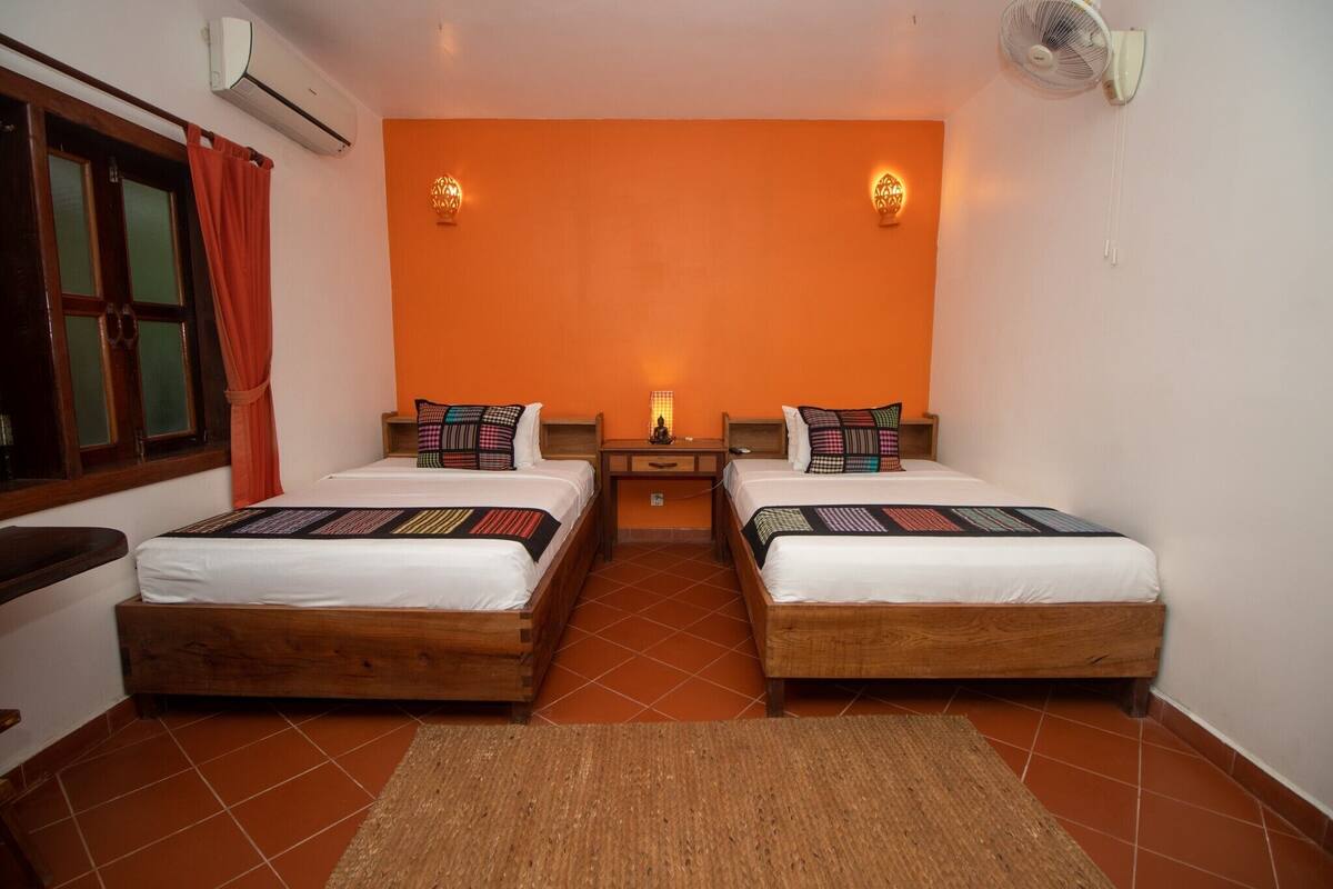 A room with two wooden beds, a small table, and a wall-mounted air conditioner.