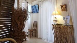 A room with exposed wooden beams, a wooden floor, a chair, a table with a lamp, and a painting on the wall.