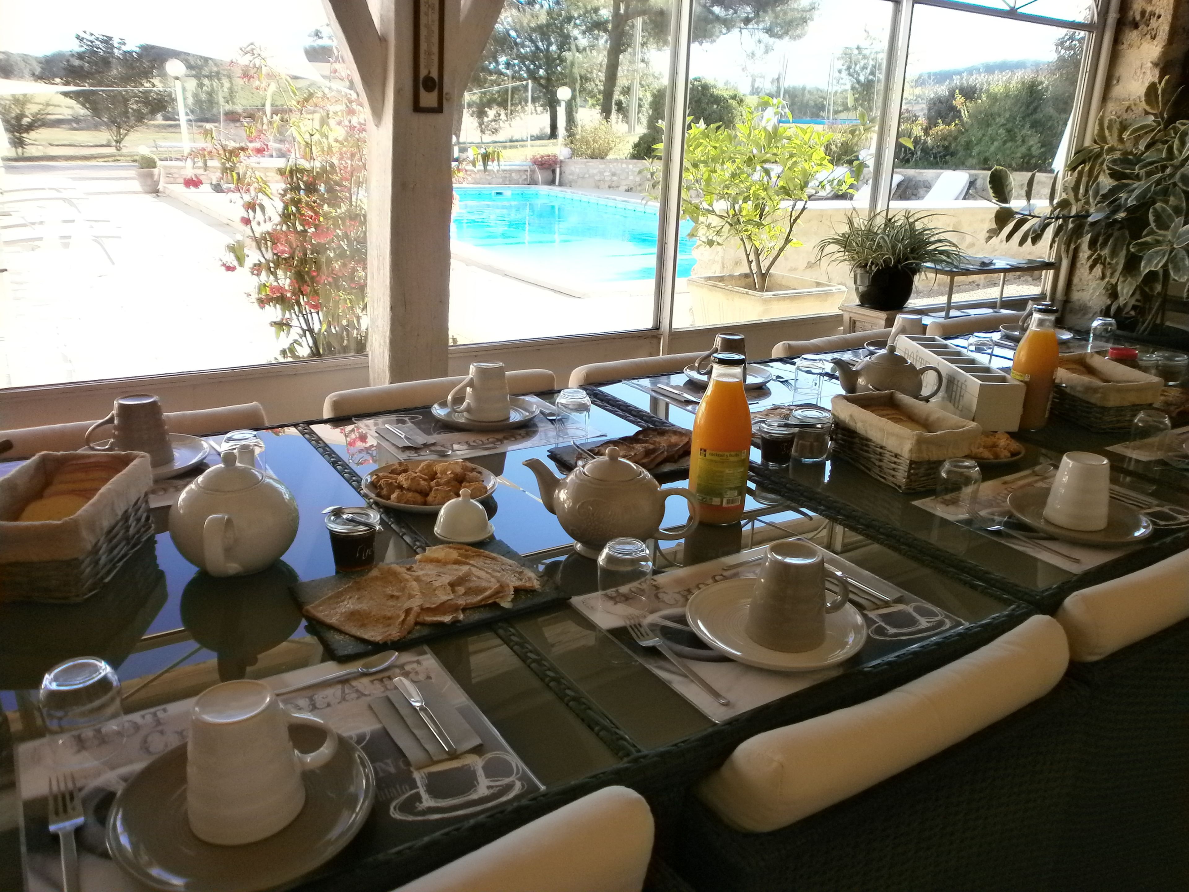 Una mesa de desayuno con diferentes platos, una botella de zumo de naranja y vistas a una piscina.