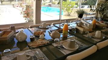 Una mesa de desayuno con diferentes platos, una botella de zumo de naranja y vistas a una piscina.
