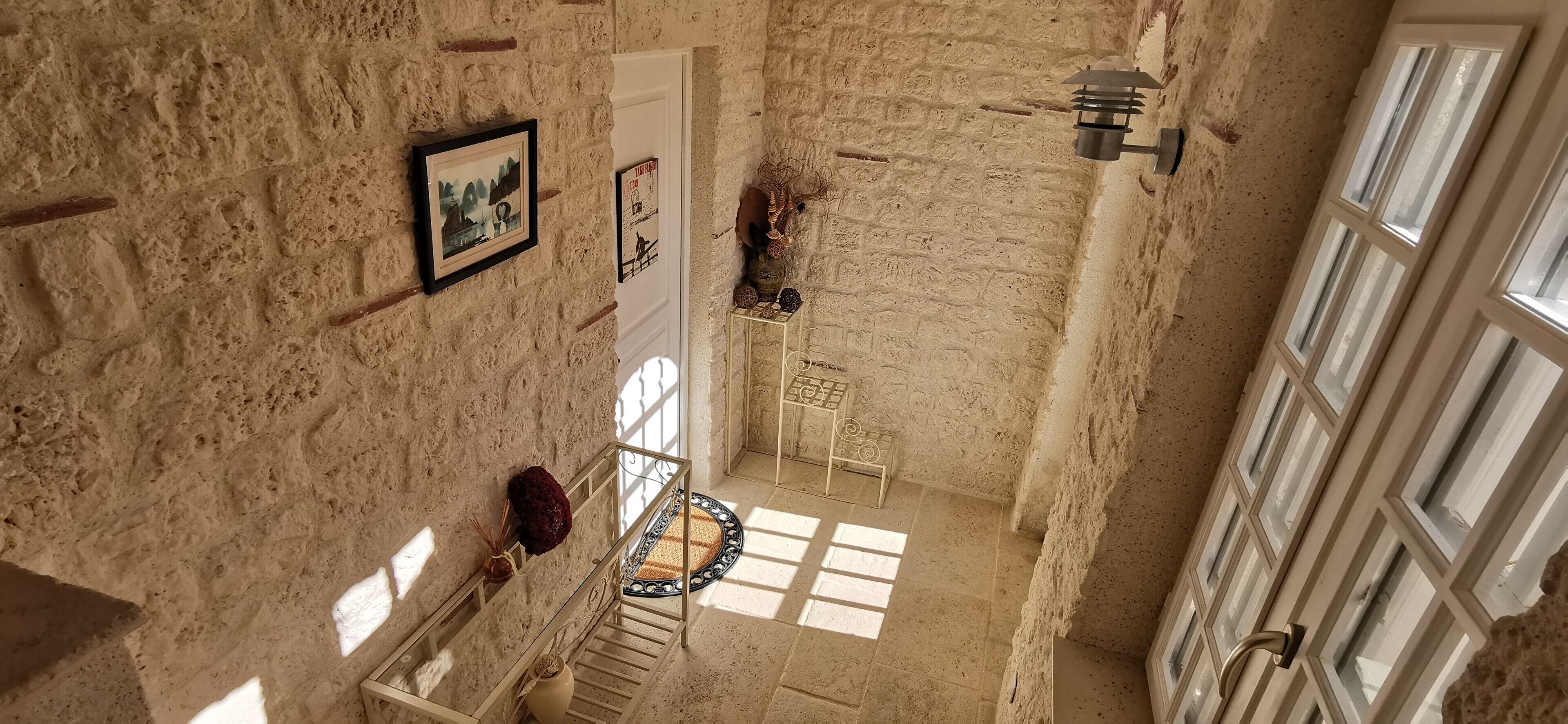 A high-ceilinged room with exposed brick walls, a staircase, and a large window allowing natural light.