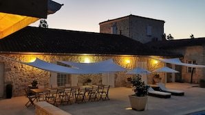 An outdoor patio with stone walls, wooden furniture, and umbrellas providing shade.