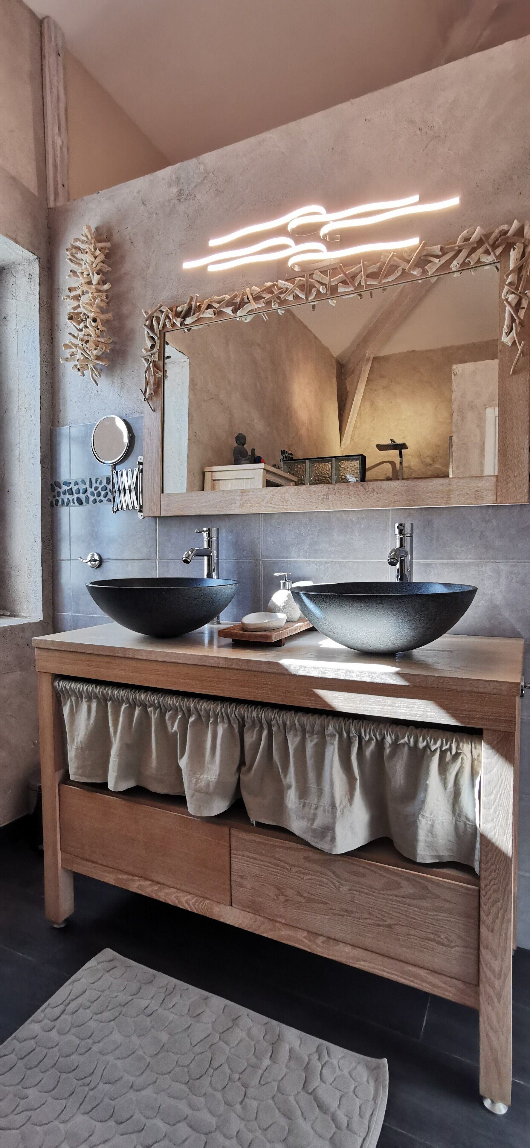 A bathroom with a wooden vanity, two vessel sinks, a mirror, and a light fixture above the mirror.